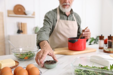 Photo of Elderly man cooking at white marble table in kitchen, closeup