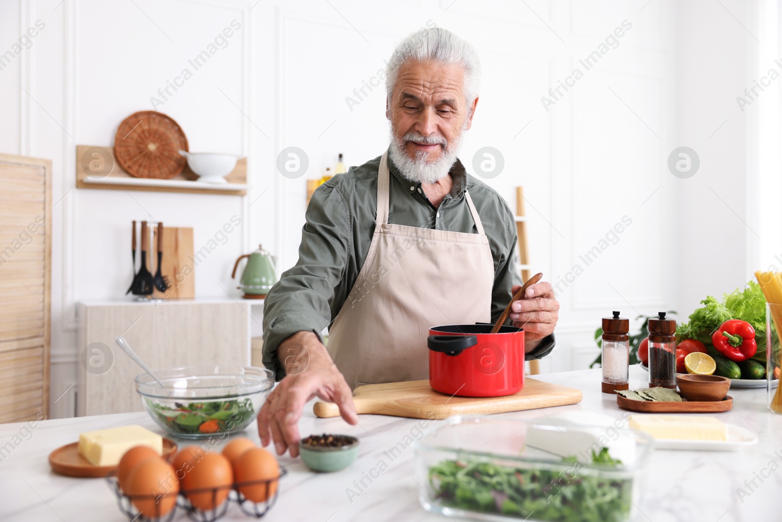 Elderly man cooking at white marble table in kitchen Photo of Elderly man cooking at white marble table in kitchen