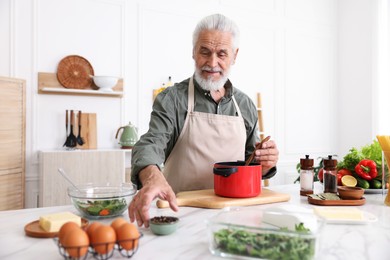 Photo of Elderly man cooking at white marble table in kitchen