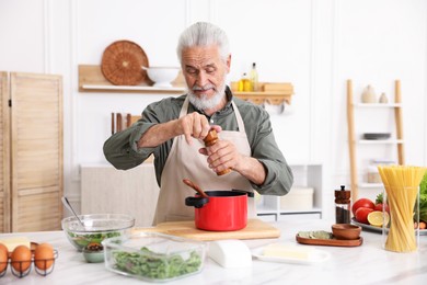 Photo of Elderly man cooking at white marble table in kitchen
