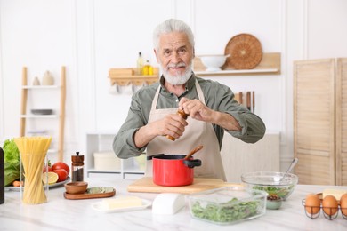 Photo of Elderly man cooking at white marble table in kitchen