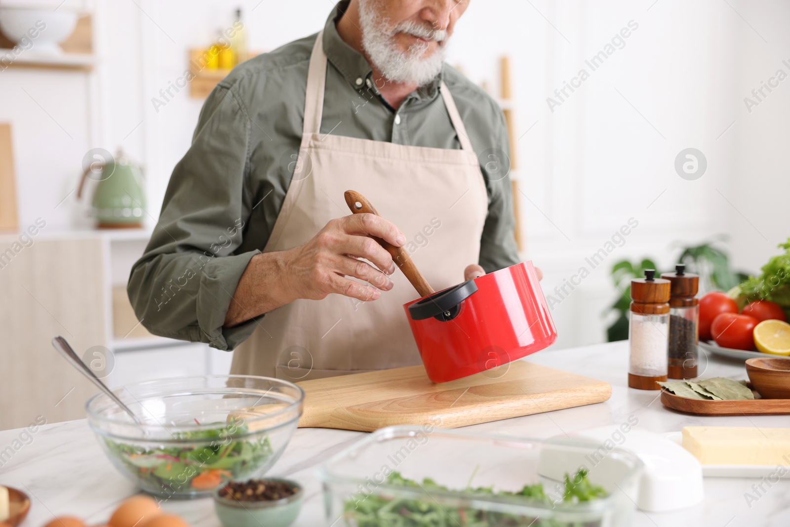 Elderly man cooking at white marble table in kitchen, closeup Photo of Elderly man cooking at white marble table in kitchen, closeup