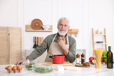 Photo of Elderly man cooking at white marble table in kitchen