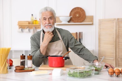 Photo of Elderly man cooking at white marble table in kitchen