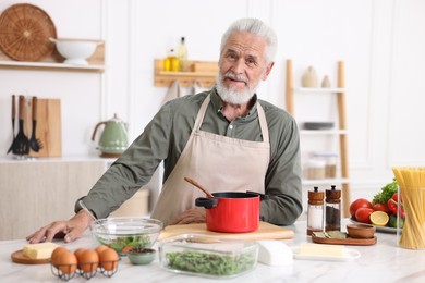 Photo of Elderly man cooking at white marble table in kitchen