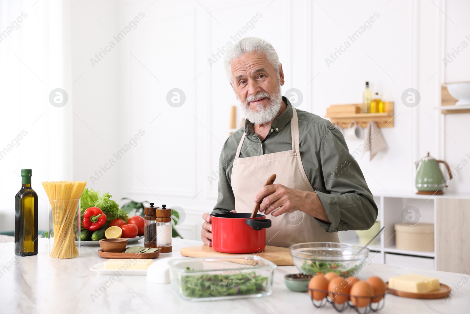 Elderly man cooking at white marble table in kitchen Photo of Elderly man cooking at white marble table in kitchen
