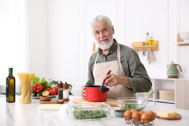 Photo of Elderly man cooking at white marble table in kitchen