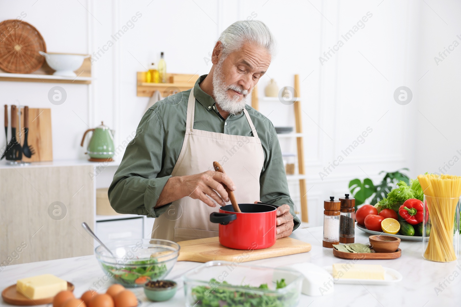 Elderly man cooking at white marble table in kitchen Photo of Elderly man cooking at white marble table in kitchen