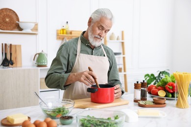 Photo of Elderly man cooking at white marble table in kitchen