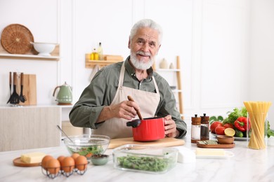Photo of Elderly man cooking at white marble table in kitchen