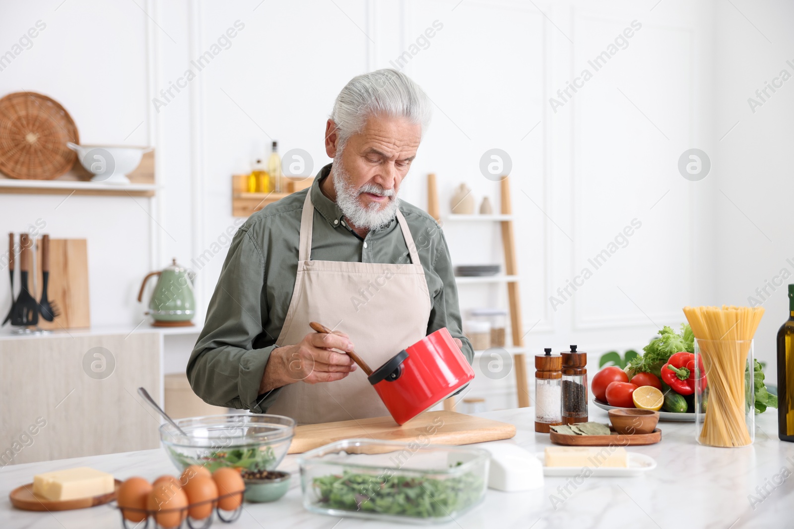 Elderly man cooking at white marble table in kitchen Photo of Elderly man cooking at white marble table in kitchen
