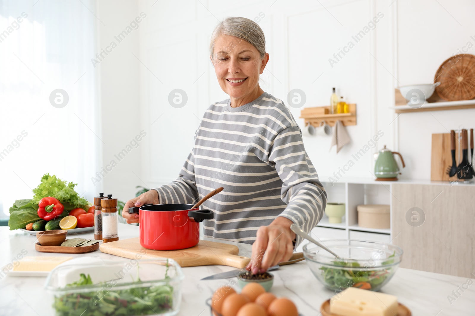 Senior woman cooking at white marble table in kitchen Photo of Senior woman cooking at white marble table in kitchen