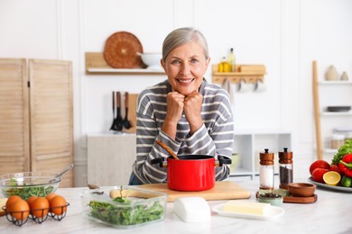Photo of Senior woman cooking at white marble table in kitchen