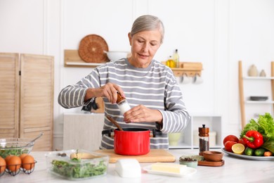 Photo of Senior woman cooking at white marble table in kitchen