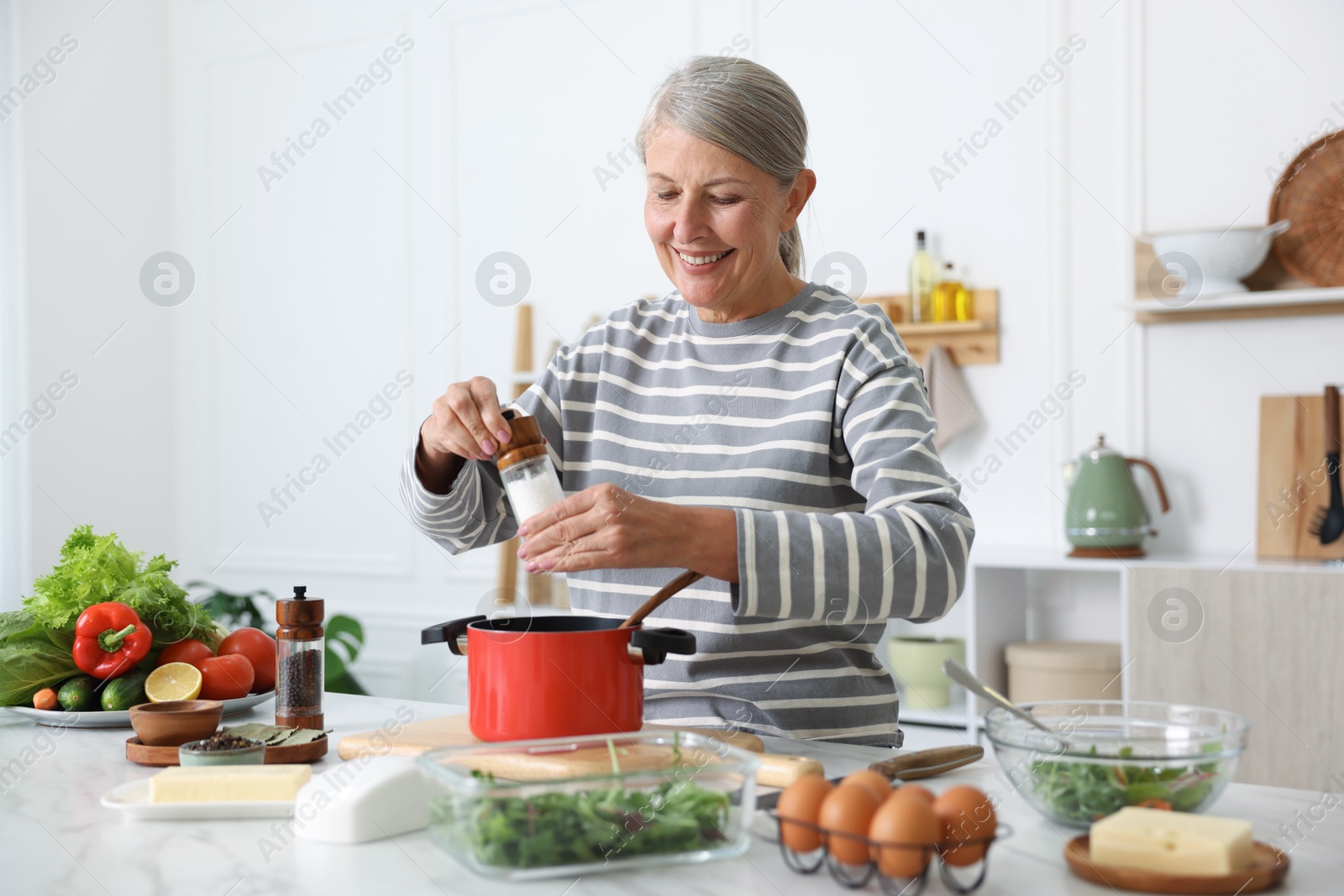 Senior woman cooking at white marble table in kitchen Photo of Senior woman cooking at white marble table in kitchen
