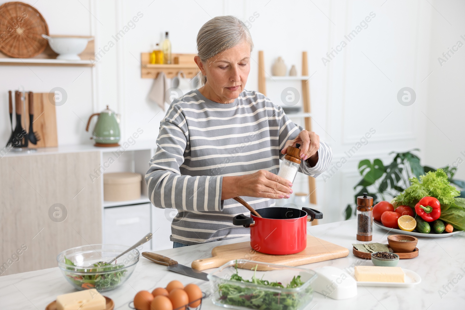 Senior woman cooking at white marble table in kitchen Photo of Senior woman cooking at white marble table in kitchen