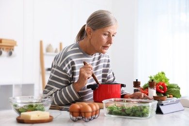 Photo of Senior woman using tablet while cooking at white marble table in kitchen
