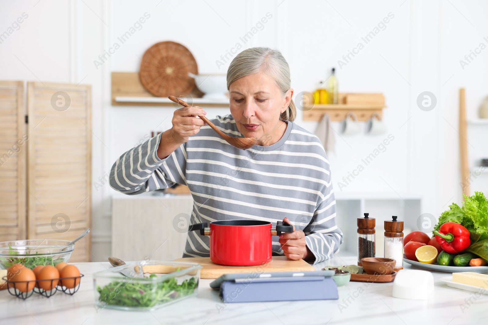 Senior woman cooking at white marble table in kitchen Photo of Senior woman cooking at white marble table in kitchen