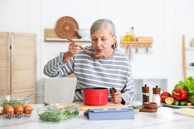 Photo of Senior woman cooking at white marble table in kitchen