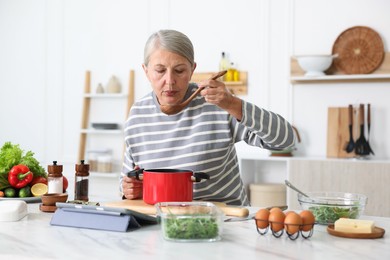 Photo of Senior woman cooking at white marble table in kitchen