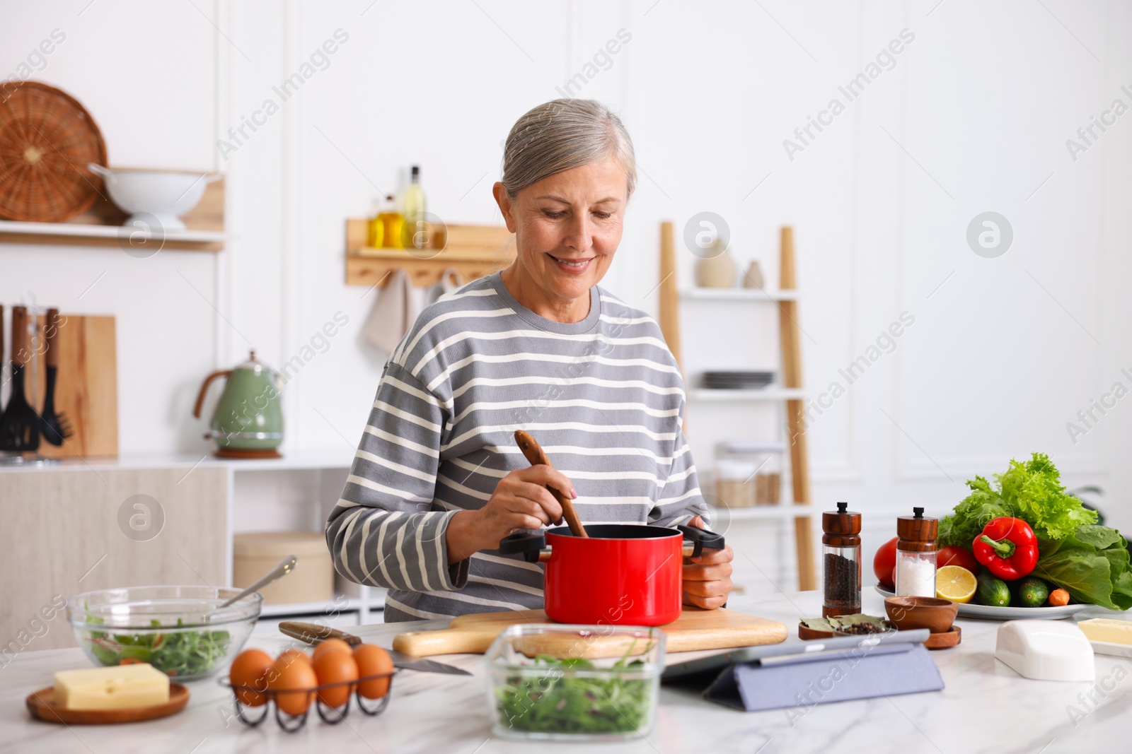 Senior woman cooking at white marble table in kitchen Photo of Senior woman cooking at white marble table in kitchen