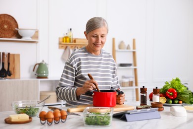 Photo of Senior woman cooking at white marble table in kitchen
