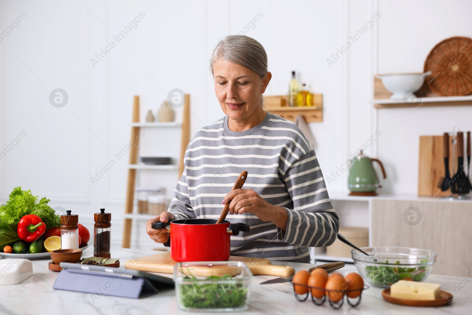 Senior woman cooking at white marble table in kitchen Photo of Senior woman cooking at white marble table in kitchen