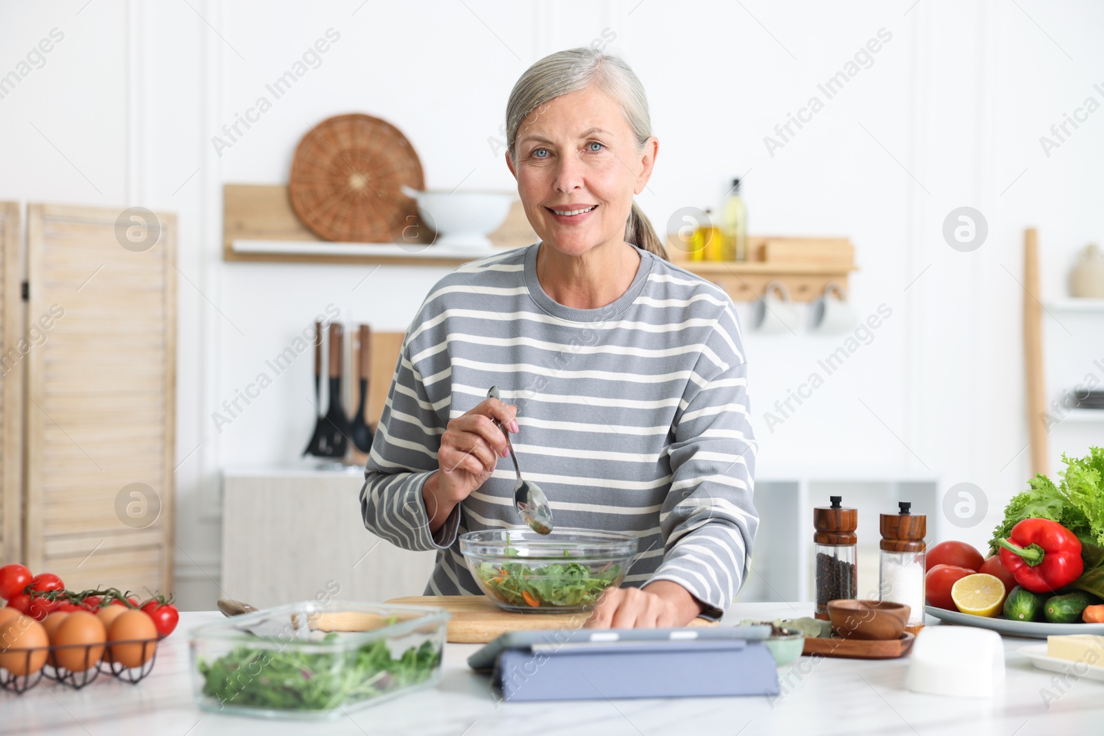 Senior woman using tablet while cooking at white marble table in kitchen Photo of Senior woman using tablet while cooking at white marble table in kitchen