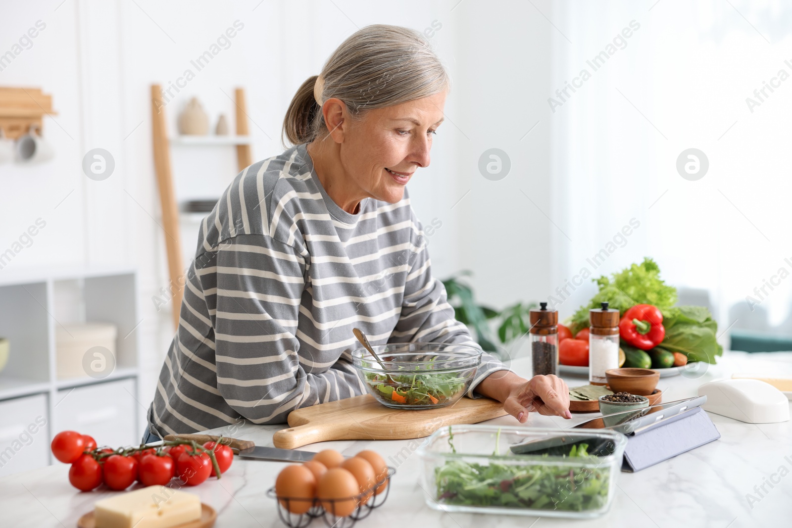 Senior woman using tablet while cooking at white marble table in kitchen Photo of Senior woman using tablet while cooking at white marble table in kitchen