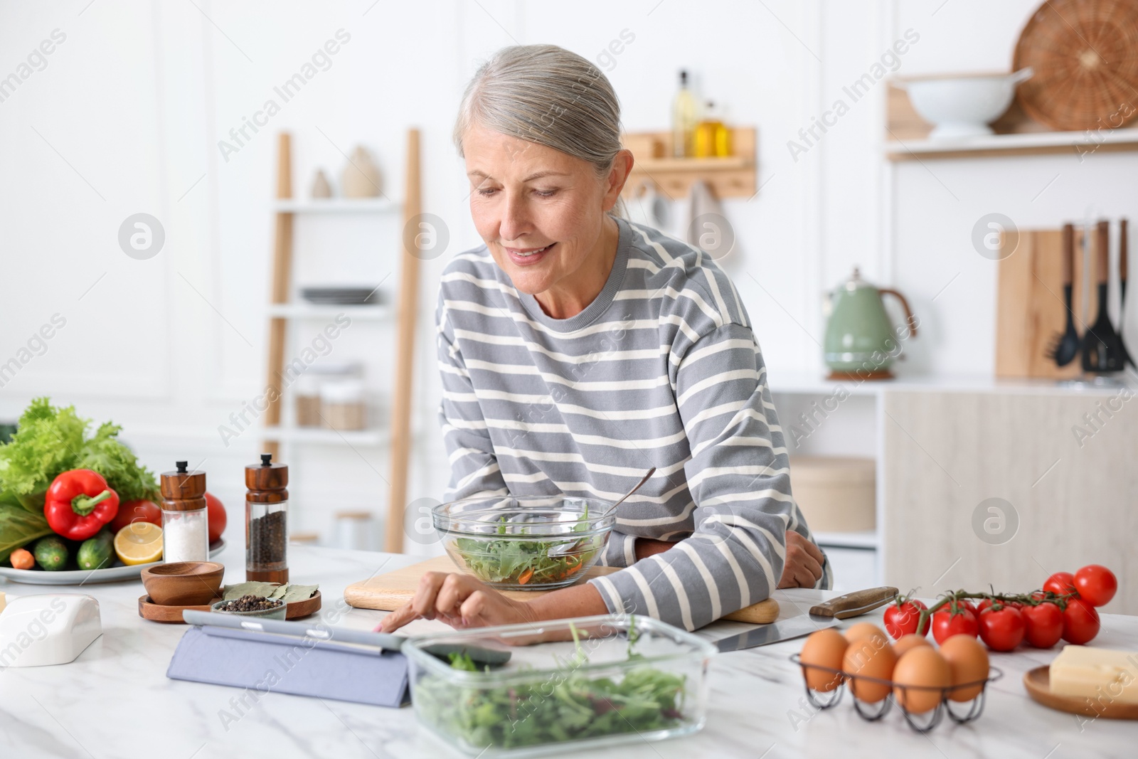 Senior woman using tablet while cooking at white marble table in kitchen Photo of Senior woman using tablet while cooking at white marble table in kitchen