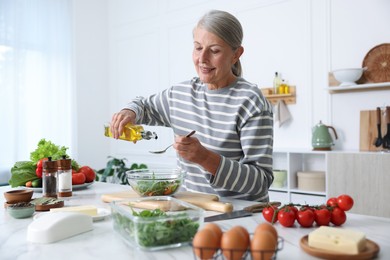 Photo of Senior woman cooking salad at white marble table in kitchen