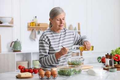 Photo of Senior woman cooking salad at white marble table in kitchen