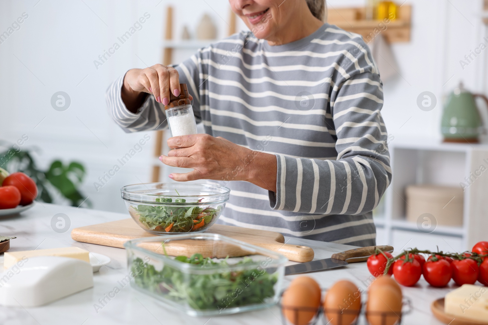 Cooking process. Senior woman adding spices to salad at white marble table in kitchen, closeup Photo of Cooking process. Senior woman adding spices to salad at white marble table in kitchen, closeup