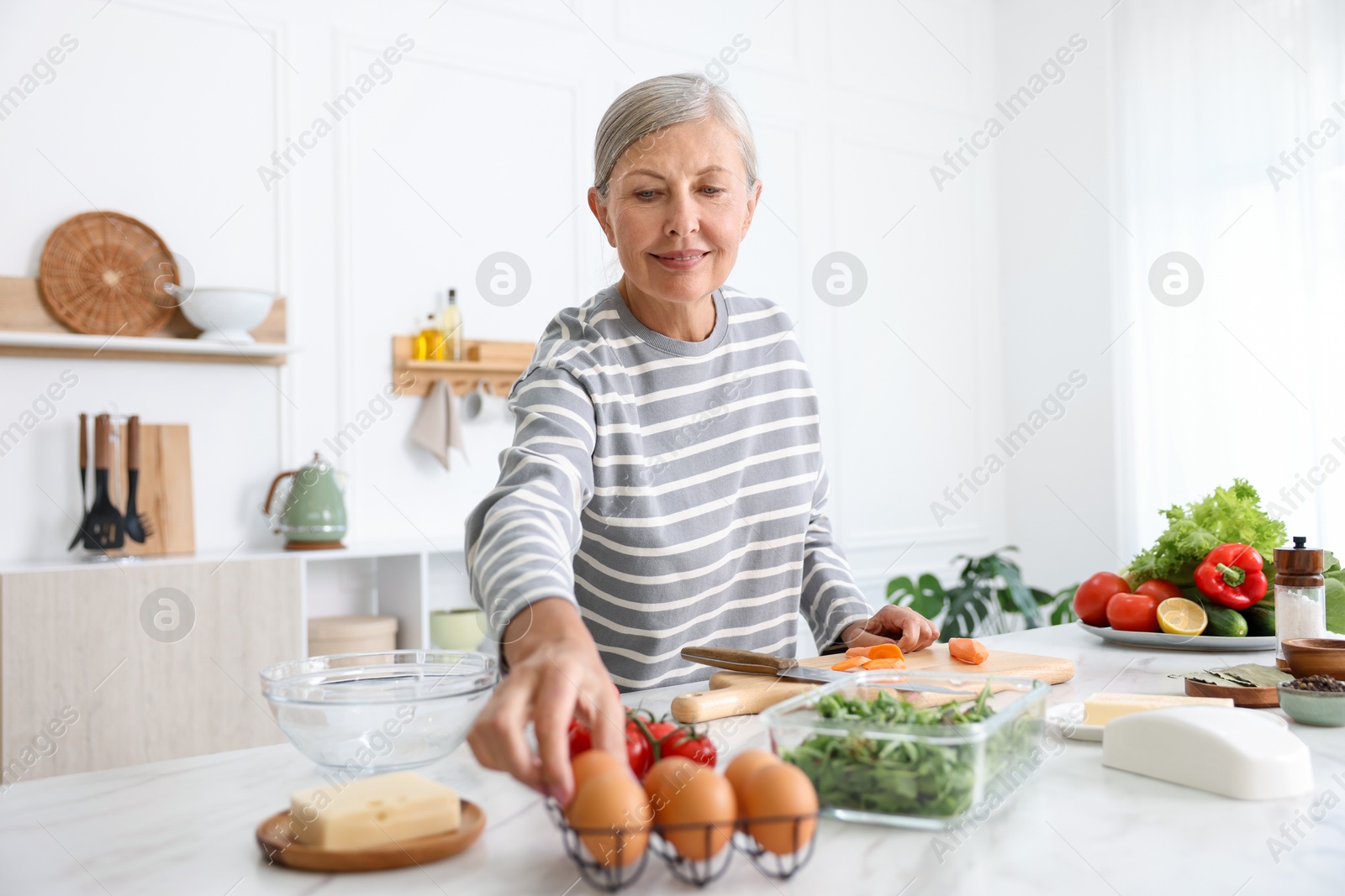 Senior woman cooking at white marble table in kitchen Photo of Senior woman cooking at white marble table in kitchen