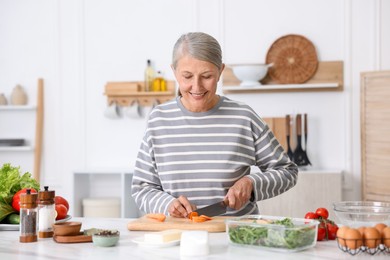 Photo of Senior woman cooking at white marble table in kitchen