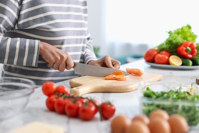 Photo of Senior woman cooking at white marble table in kitchen, closeup