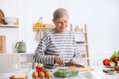 Photo of Senior woman cooking at white marble table in kitchen