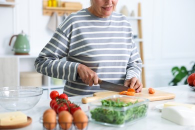 Photo of Senior woman cooking at white marble table in kitchen, closeup