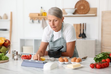 Photo of Senior woman using tablet while cooking at white marble table in kitchen