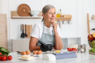 Photo of Senior woman cooking at white marble table in kitchen