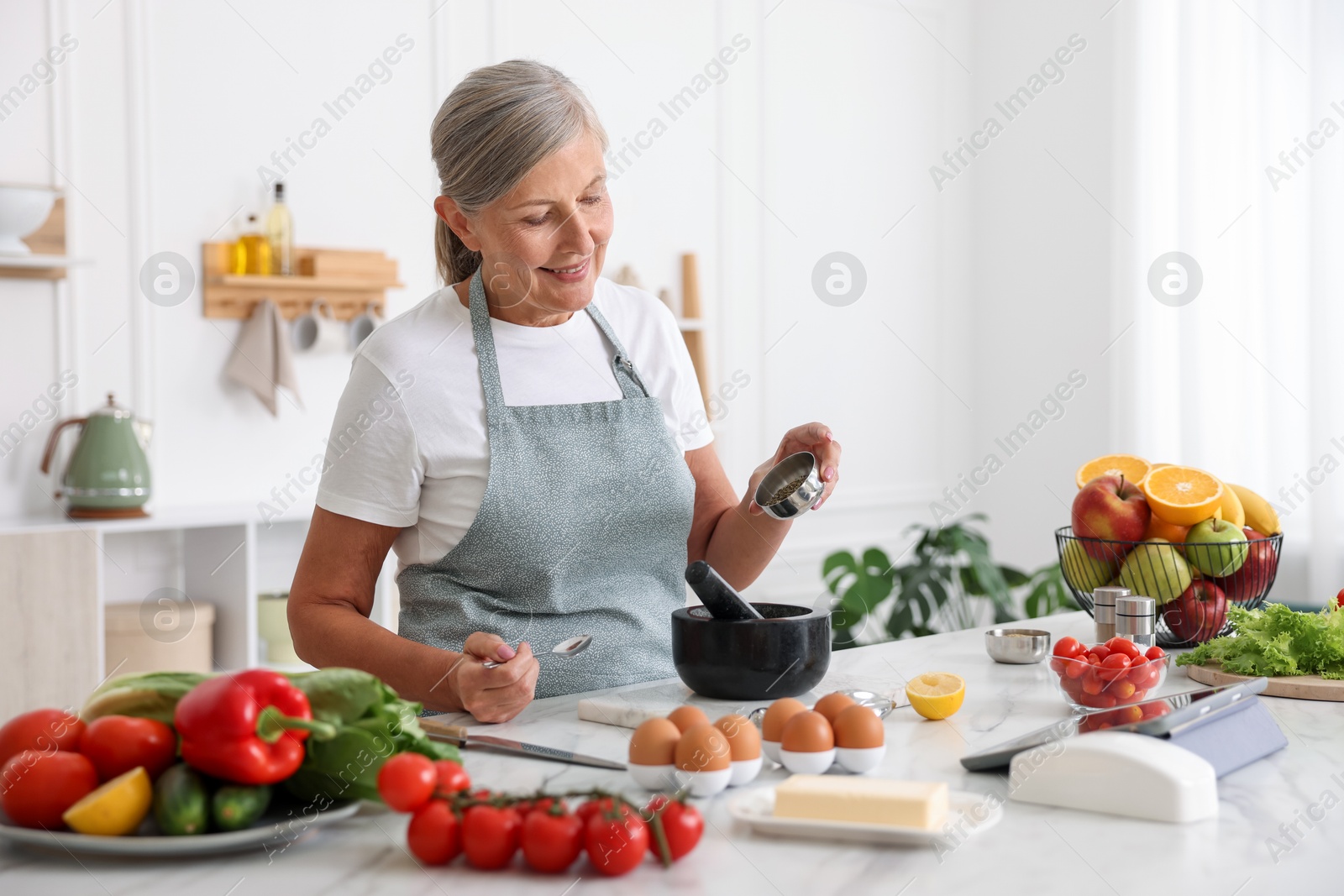 Senior woman cooking at white marble table in kitchen Photo of Senior woman cooking at white marble table in kitchen