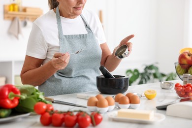 Photo of Senior woman cooking at white marble table in kitchen, closeup