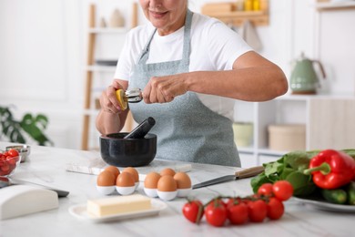 Photo of Senior woman cooking at white marble table in kitchen, closeup