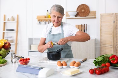 Photo of Senior woman cooking at white marble table in kitchen