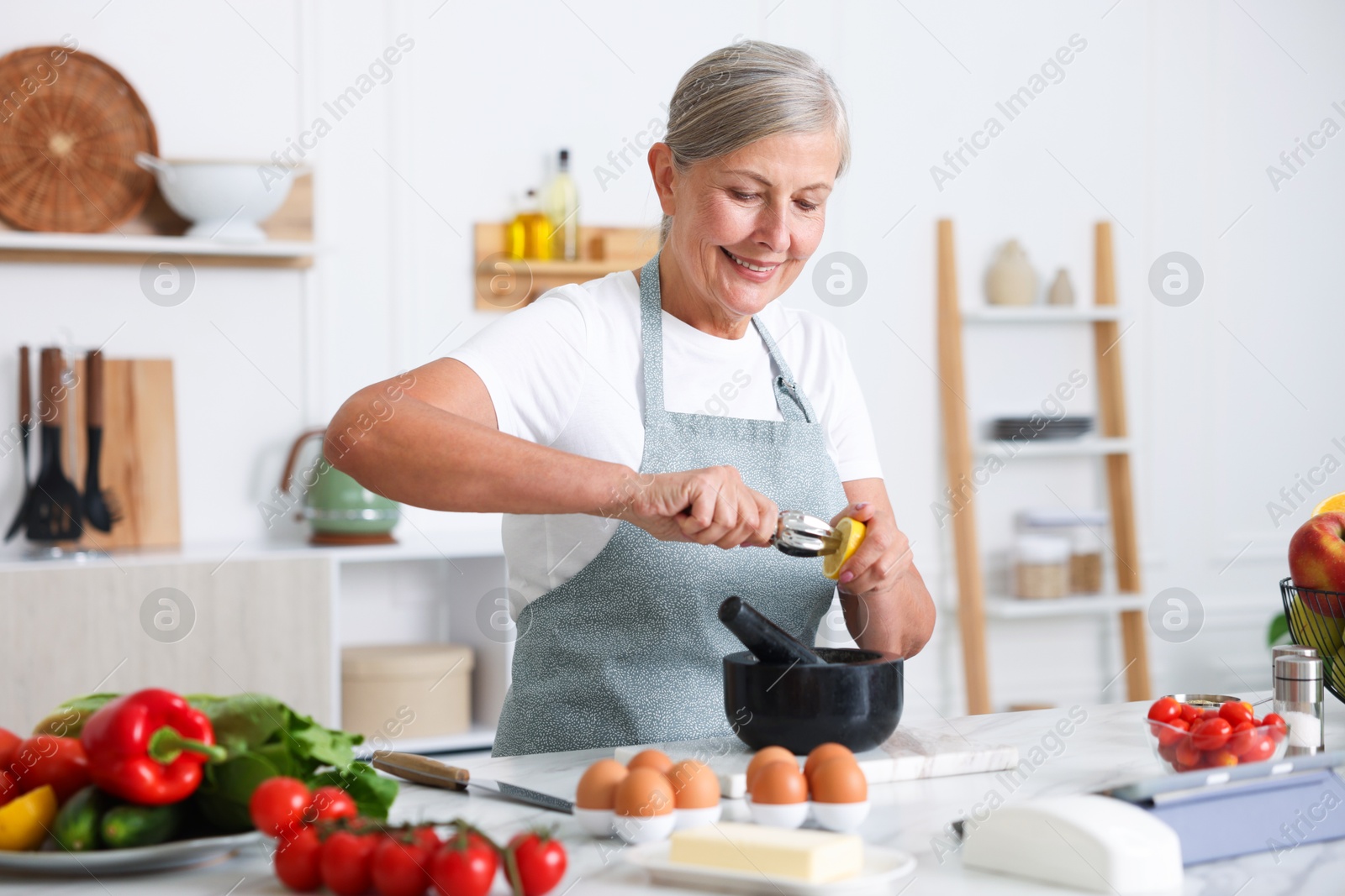 Senior woman cooking at white marble table in kitchen Photo of Senior woman cooking at white marble table in kitchen
