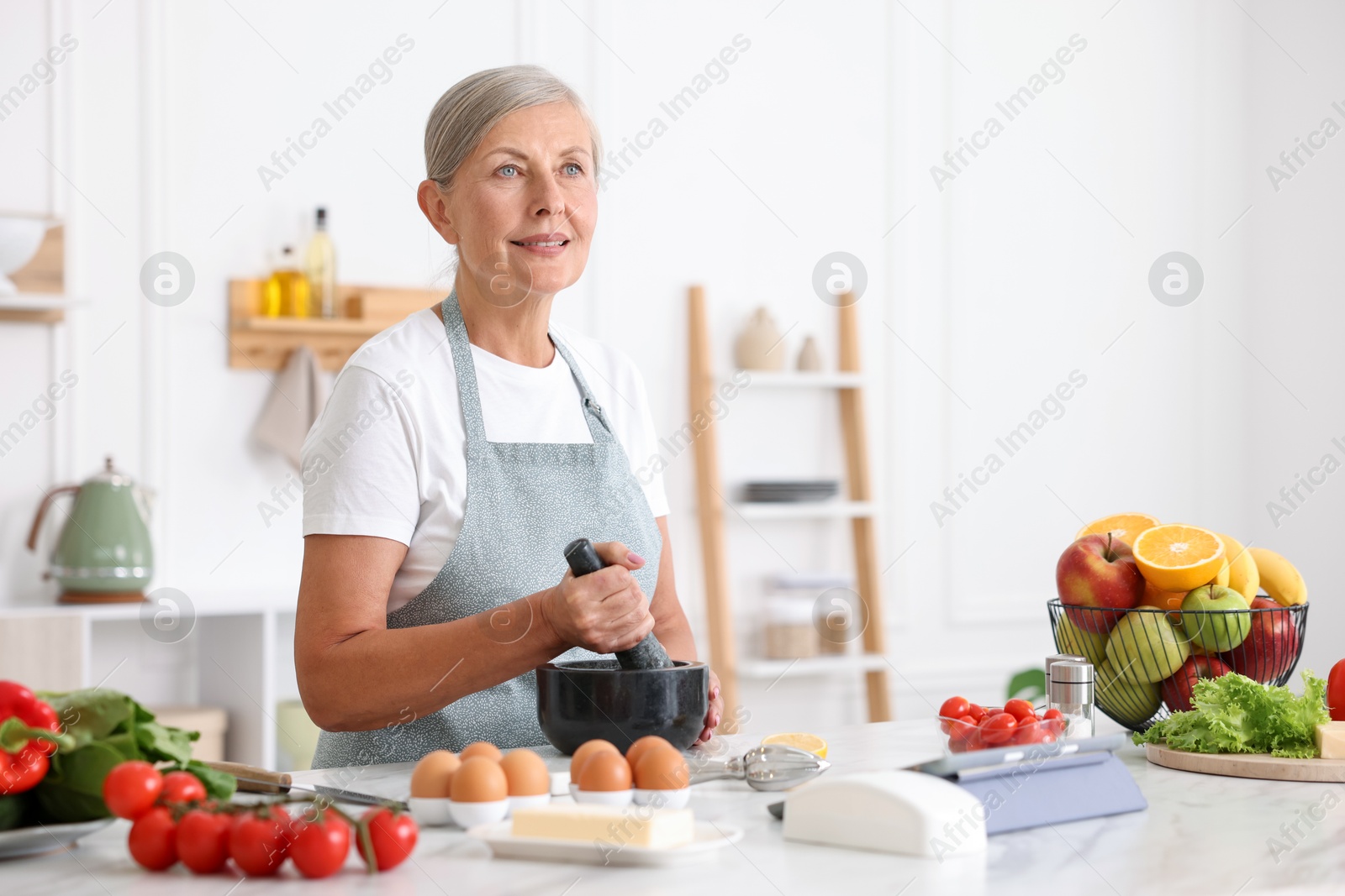 Senior woman cooking at white marble table in kitchen Photo of Senior woman cooking at white marble table in kitchen