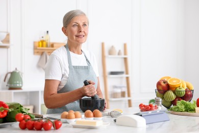 Photo of Senior woman cooking at white marble table in kitchen