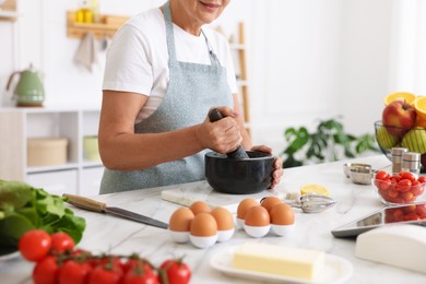 Photo of Senior woman cooking at white marble table in kitchen