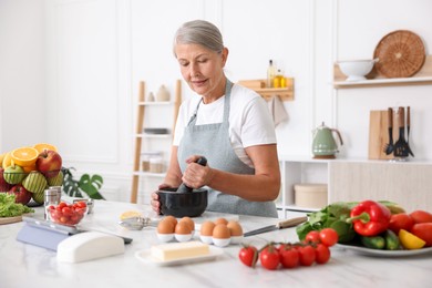 Photo of Senior woman cooking at white marble table in kitchen