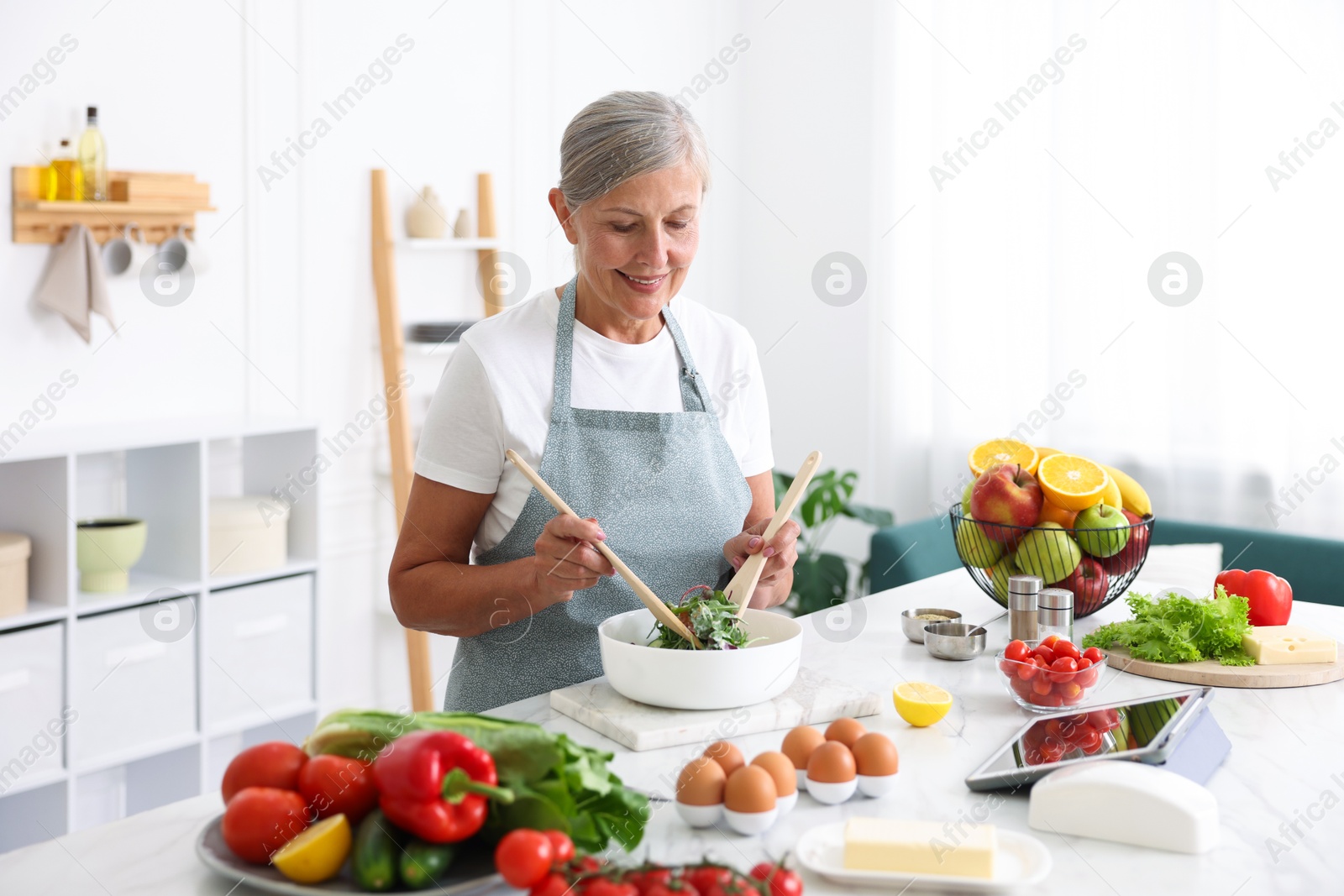 Photo of Senior woman cooking salad at white marble table in kitchen